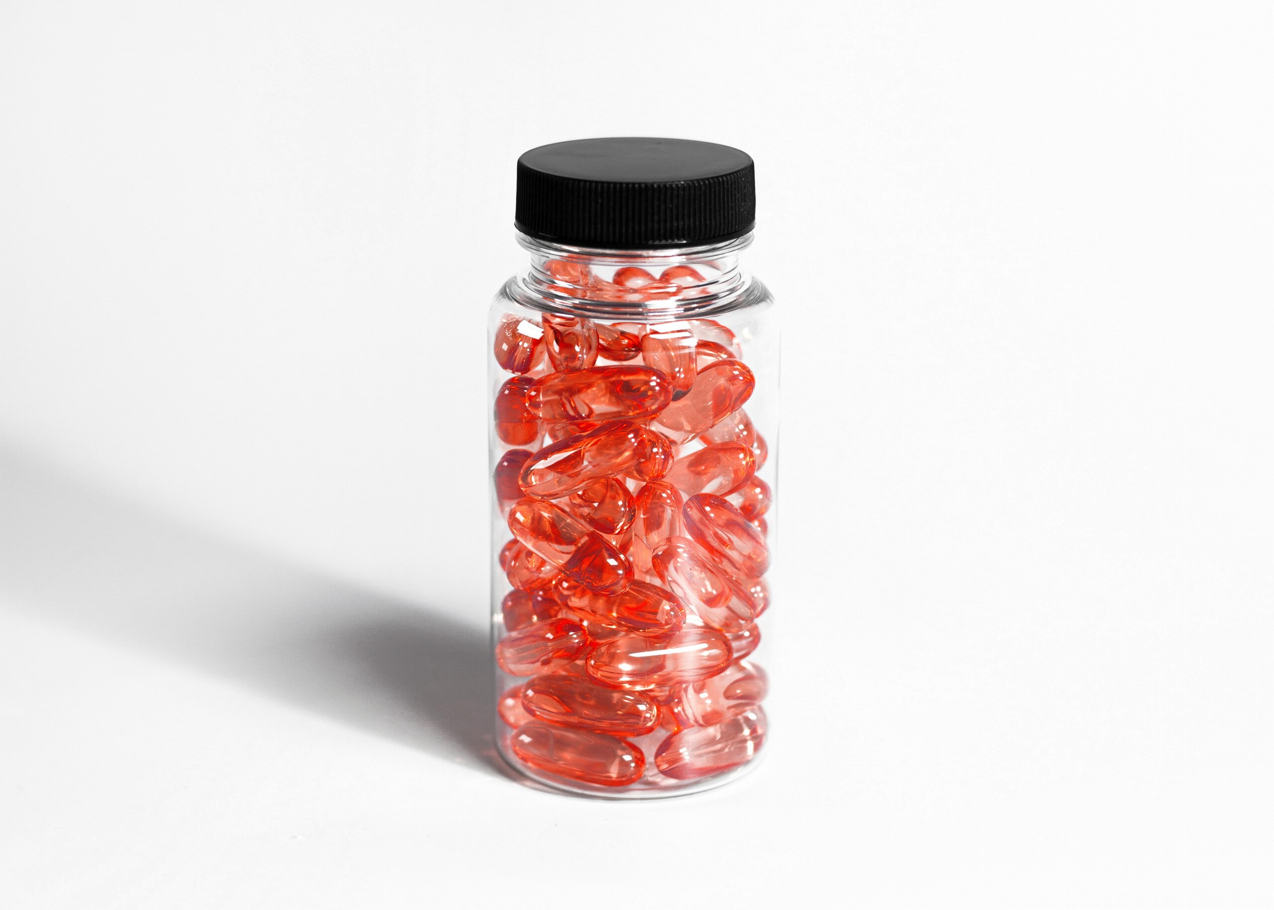 A pill bottle containing red tablets and made from recycled plastics